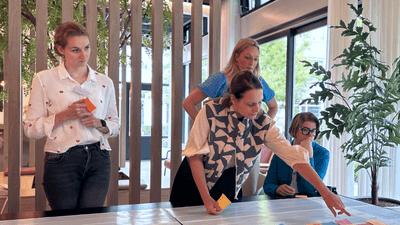 Mensen buigen zich over een tafel met post-its. Ze kijken allemaal naar het vel op tafel.