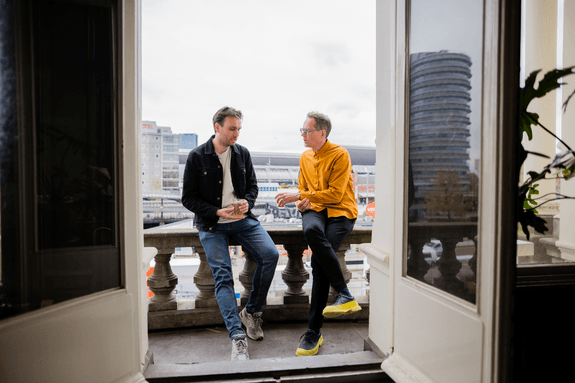 Twee mannen zitten op een balkon bij Norday, GRRR en kijken uit over Amsterdam