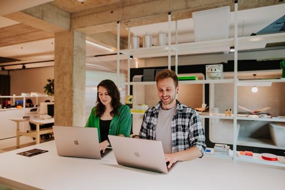 Een man en vrouw staan aan een tafel met hun laptop open geklapt