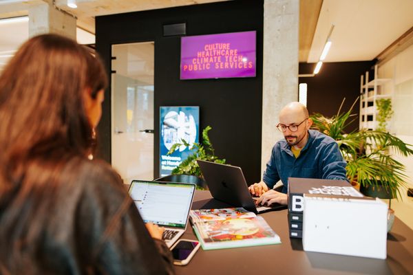 Man en vrouw zitten tegenover elkaar aan een bureau. Ze kijken allebei naar hun laptop.