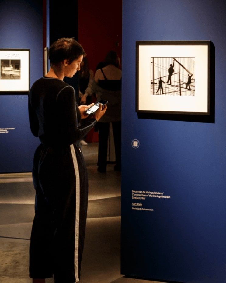 Vrouw staand voor een kunstwerk in museum met een telefoon in haar hand. Fotomuseum