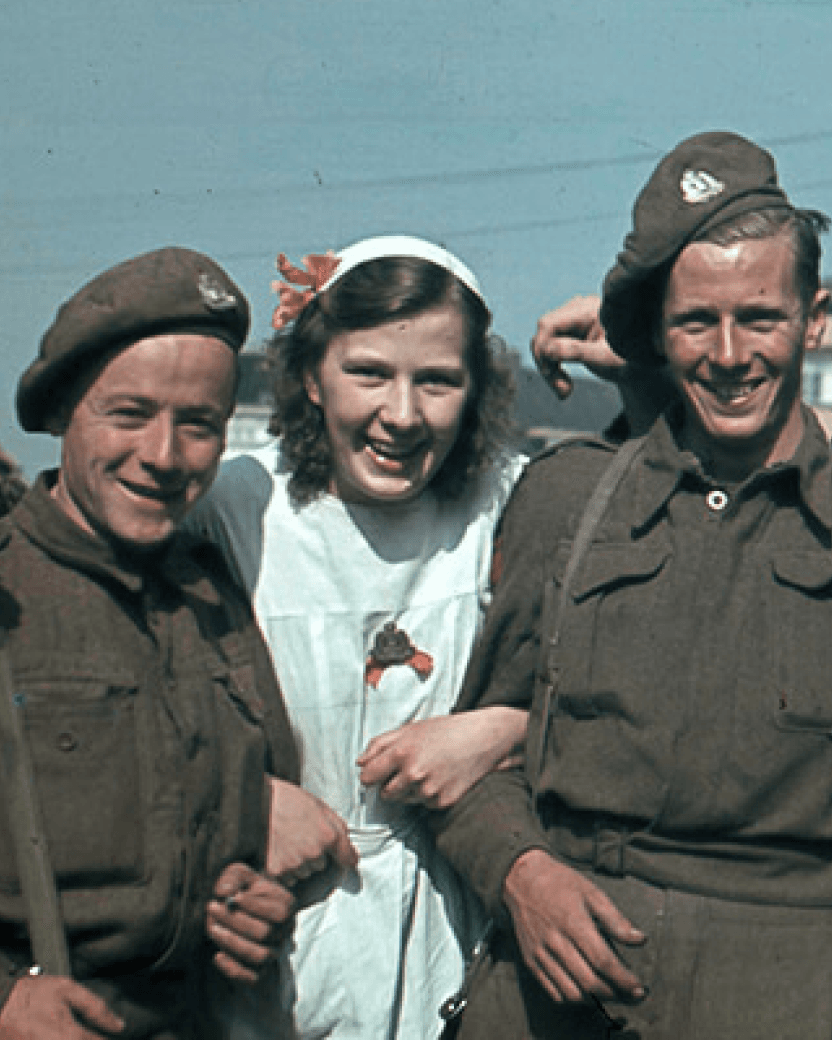 Een vrouw staat tussen twee soldaten uit de Tweede Wereldoorlog in. Ze lachen in de camera.